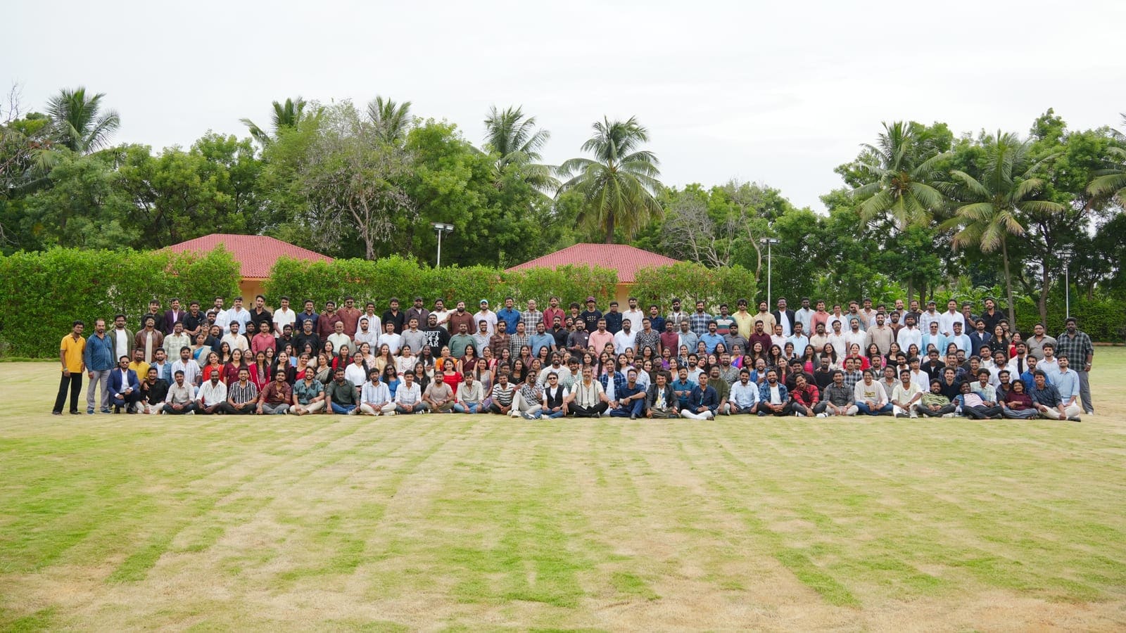 The whole Praval team assembled on a lawn for a group photograph, with palm trees and the pavilion roofs behind them