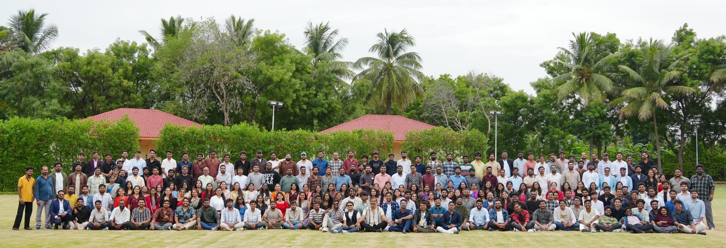 The whole Praval team assembled on a lawn for a group photograph, with palm trees and the pavilion roofs behind them